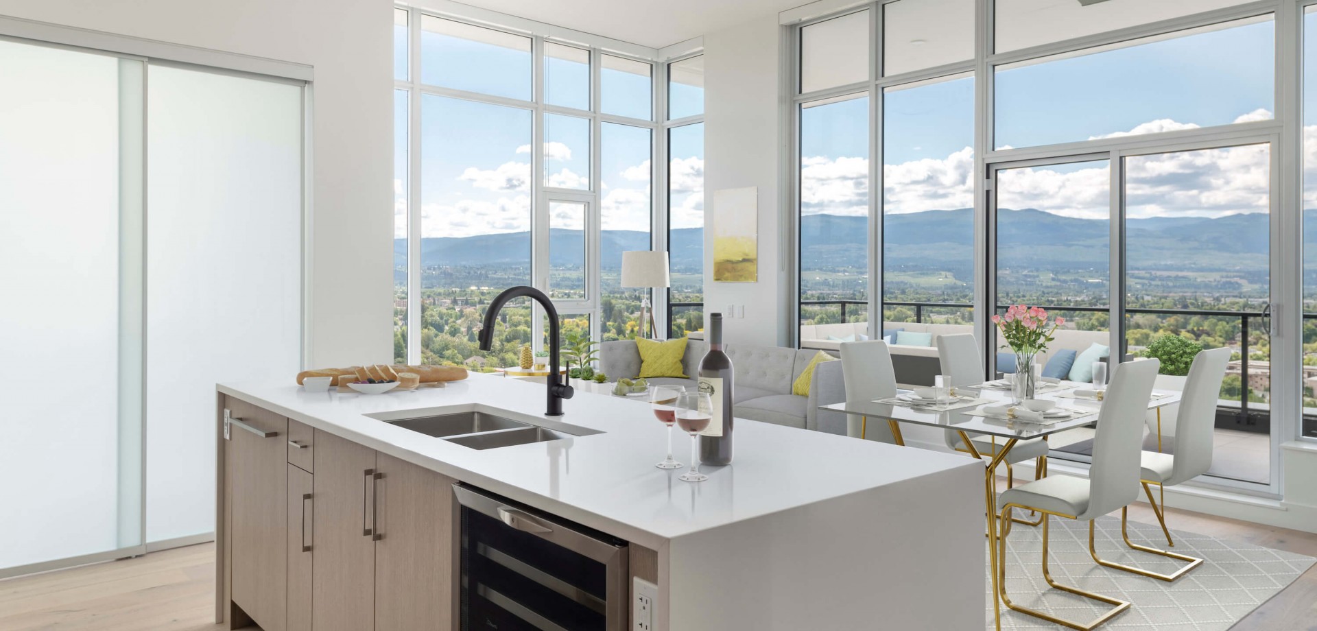 Ella Penthouse kitchen in Kelowna; apartment kitchen with island, dinning table, white chair and skyscraper facing outside during the day