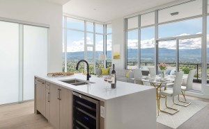 Ella Penthouse kitchen in Kelowna; apartment kitchen with island, dinning table, white chair and skyscraper facing outside during the day