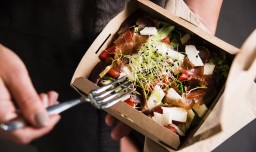 Woman's hand is holding a take away fresh salad in a lunch box. Gourmet conception.